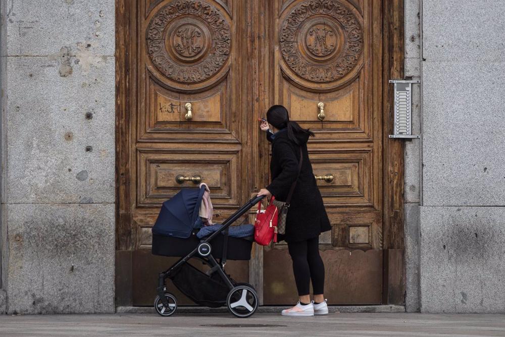 Archivo - Una mujer frente a un portal con un carrito de bebé. Archivo