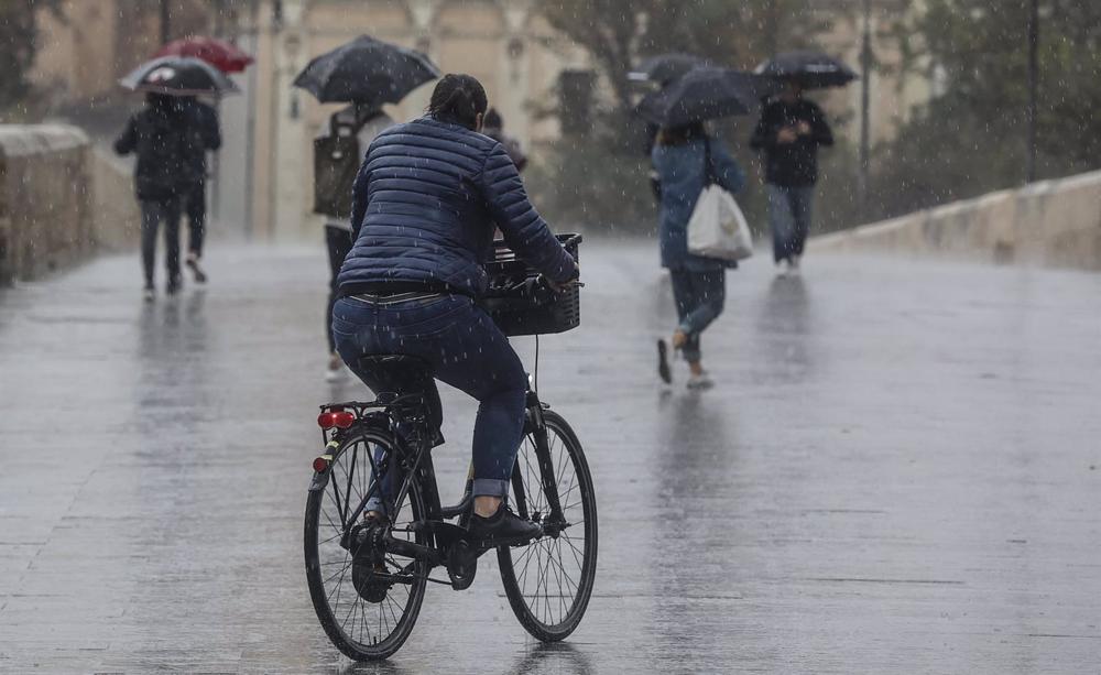 Archivo - Una persona circula en bicicleta bajo la lluvia en Valencia. Archivo