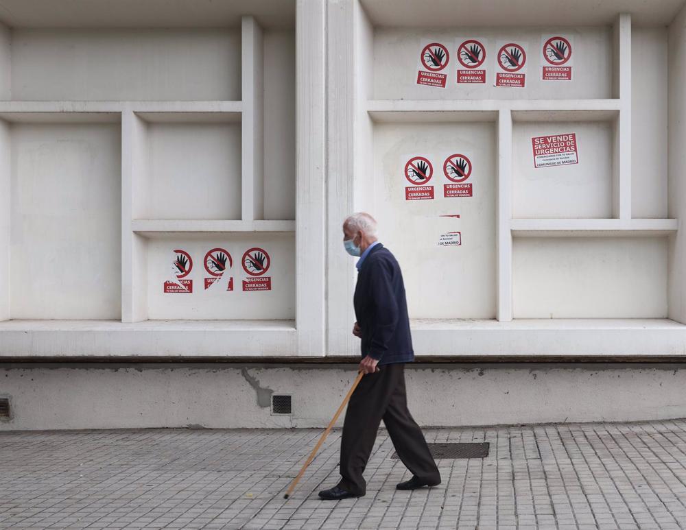 Un hombre mayor con mascarilla y bastón camina delante del Centro de Salud Pavones, Un
