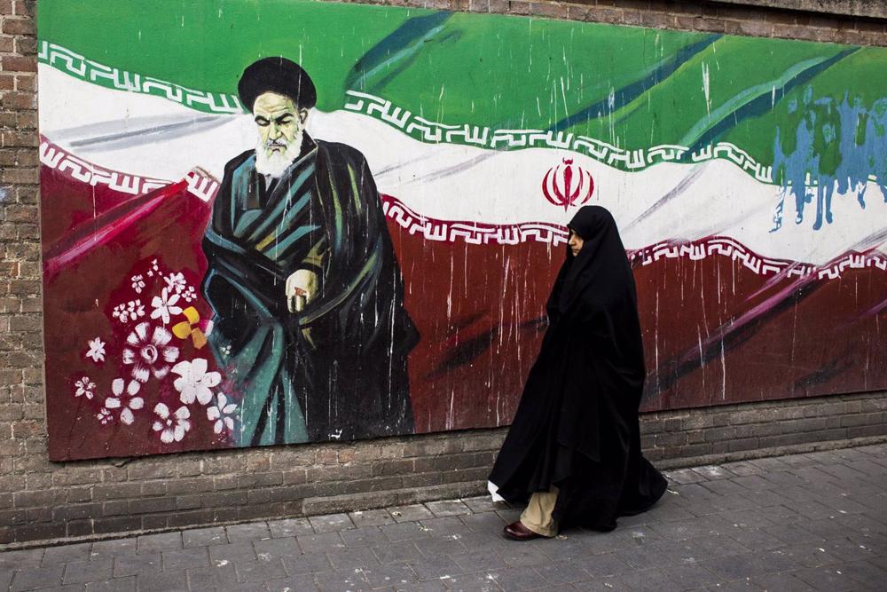 Eine Frau steht neben einem Wandgemälde mit der iranischen Flagge und Ayatollah Ruhollah Khomeini in Teheran. Eine