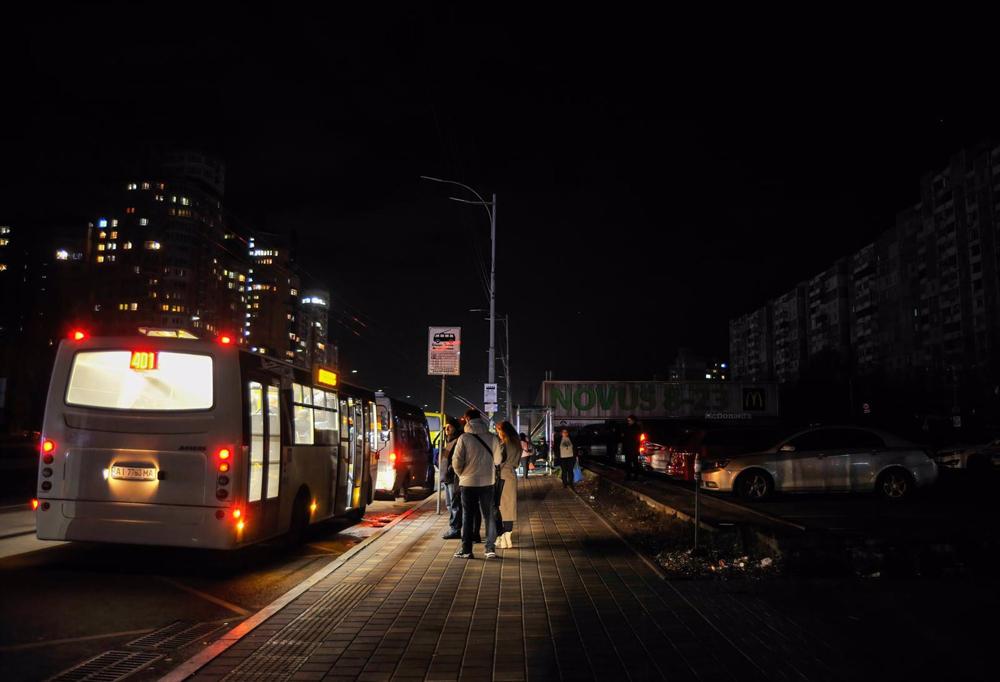 People standing at a public transport stop in an unlit Kiev. People