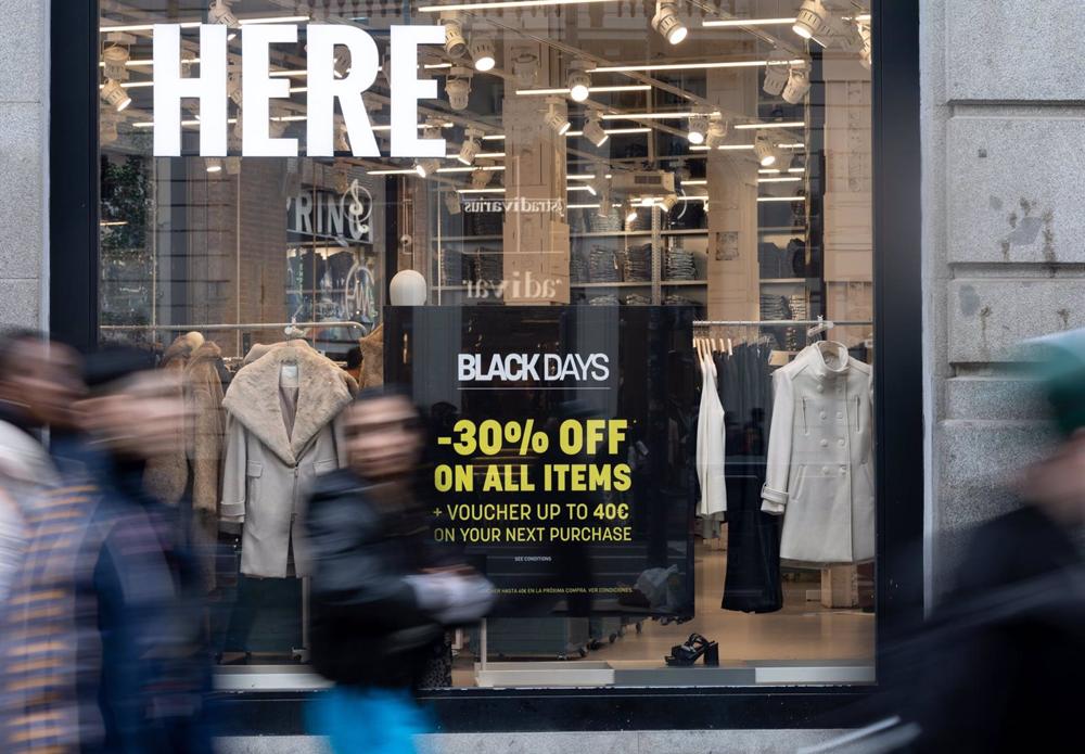 Varias personas pasan por delante de los comercios que anuncian los descuentos del Black Friday Varias