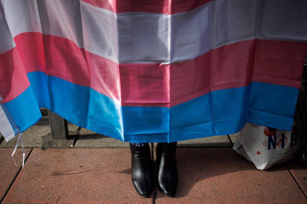 Archivo - Los zapatos de una mujer debajo de una bandera trans durante una concentración. Archivo
