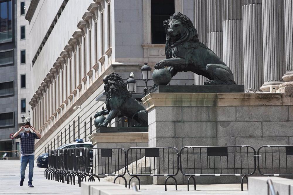 Archivo - Un hombre se coloca una mascarilla mientras camina por delante de la fachada del Congreso de los Diputados, que este miércoles vota por cuarta vez una prórroga del estado de alarma decretado frente al coronavirus, que no tiene riesgo de revocars Archivo