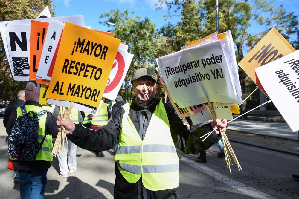 Un hombre sujeta varias pancartas en una manifestación de pensionistas Un
