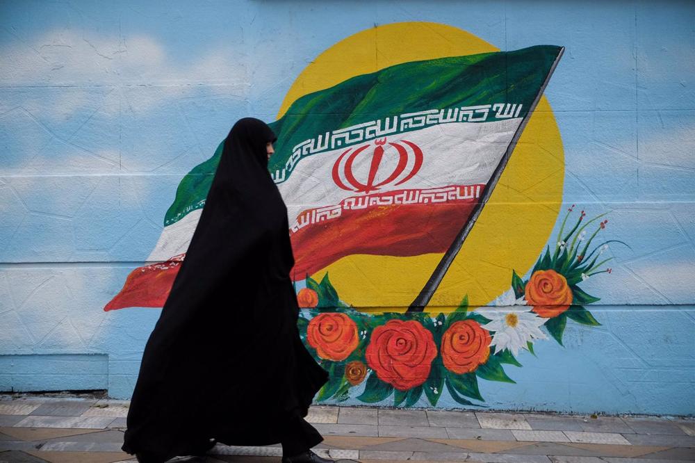 File - A woman in a chador walks past a mural with the Iranian flag in Tehran. File