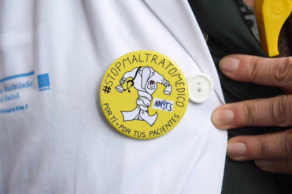 Un sanitario con una chapa en la que se lee '#StopMaltratoMédico. Por ti - Por tus pacientes' Un