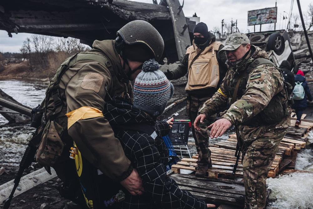 File - Soldiers help a child cross the river, March 7, 2022, in Irpin, Ukraine. File
