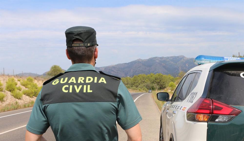 Archivo - Un agente de la Guardia Civil junto a un vehículo en una carretera. Archivo