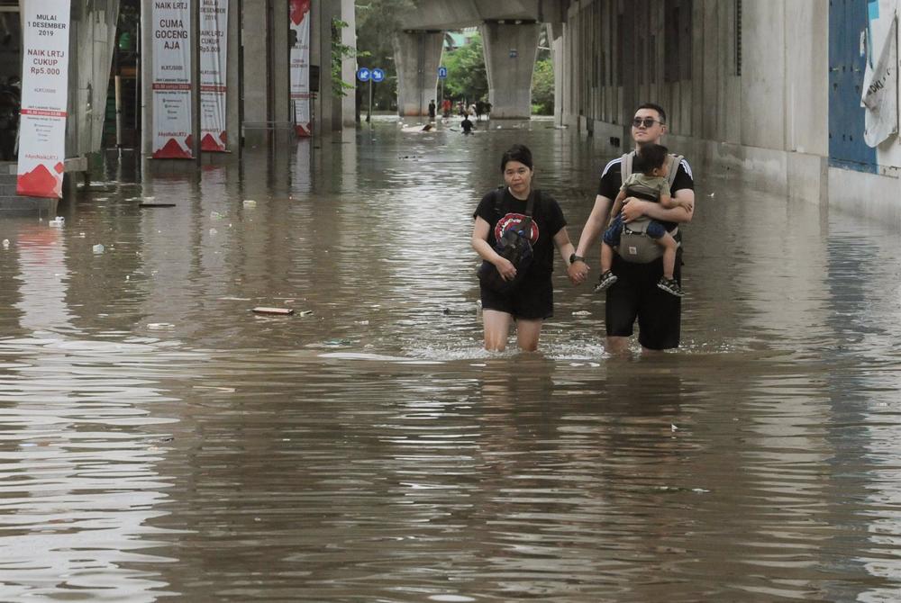 Archivo - Una pareja camina pro una calle inundada en Indonesia. Archivo