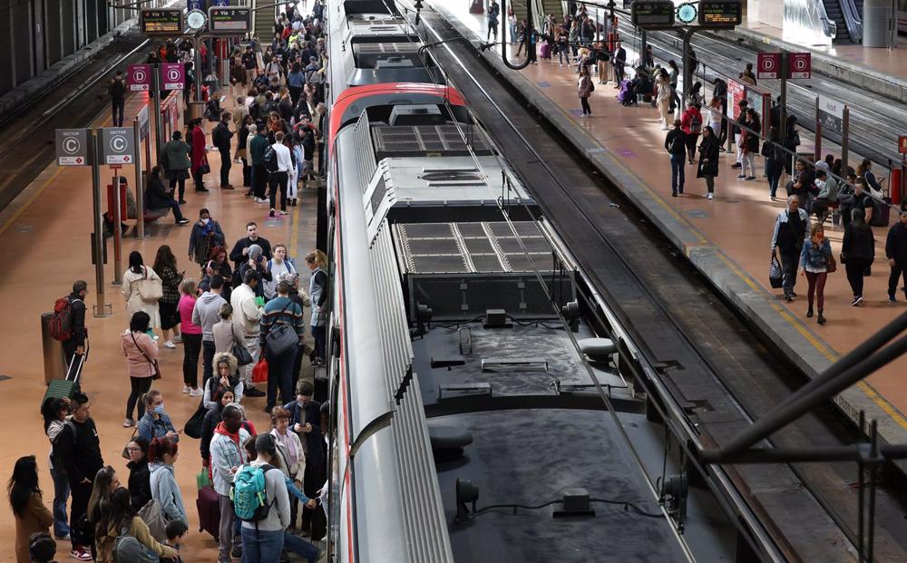 Numerosas personas con maletas esperan en el andén la salida de un tren, en la estación Almudena Grandes-Atocha Cercanías Numerosas