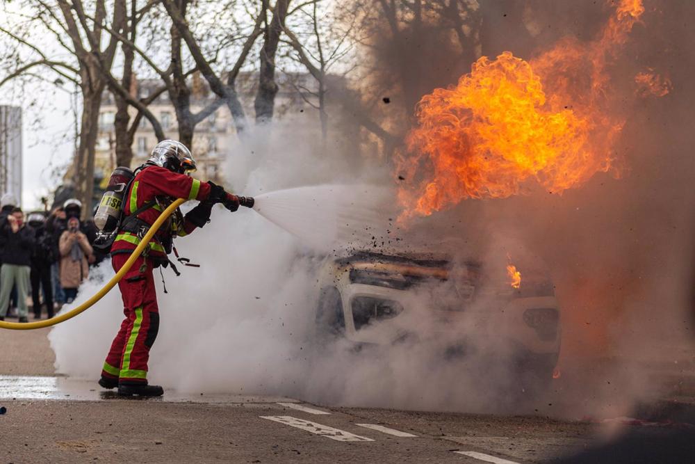 Un bombero apaga el incendio de un coche durante las protesta contra la reforma de las pensiones en París Un