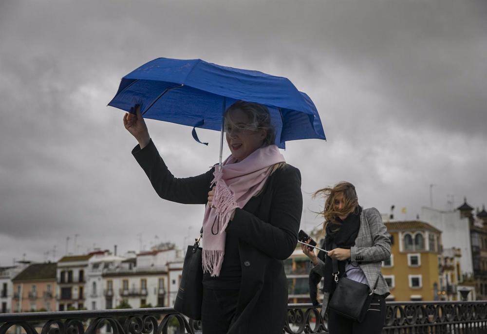 Archivo - Dos mujeres intentan protegerse del viento con su paragüas mientras caminan por el Puente de Isabel II, en Sevilla (Andalucía). Archivo