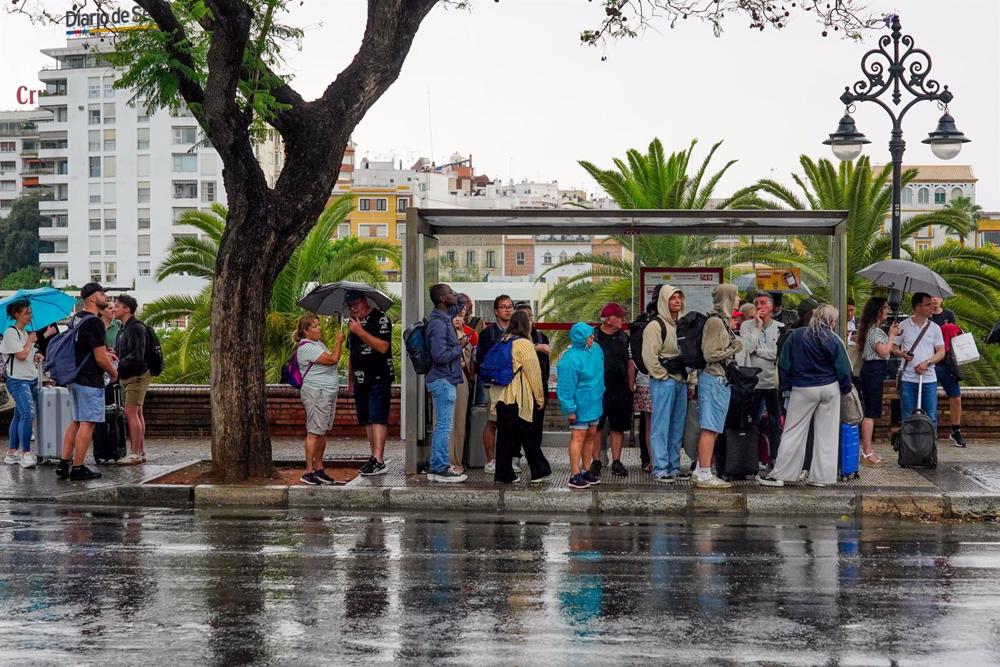 Turistas refugiado por la lluvia en una parada de autobús, a 18 de mayo de 2023, en Sevilla, (Andalucía, España). La Agencia Estatal de Meteorología acierta y llueve sobre Sevilla. Esta medio día a comenzado a llover según lo previsto por la Aemet. Turistas