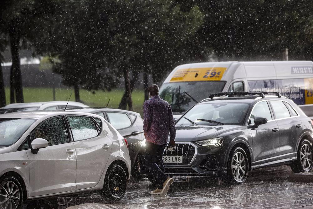 Archivo - Un hombre camina entre varios coches mientras la lluvia cae en imagen de archivo Archivo